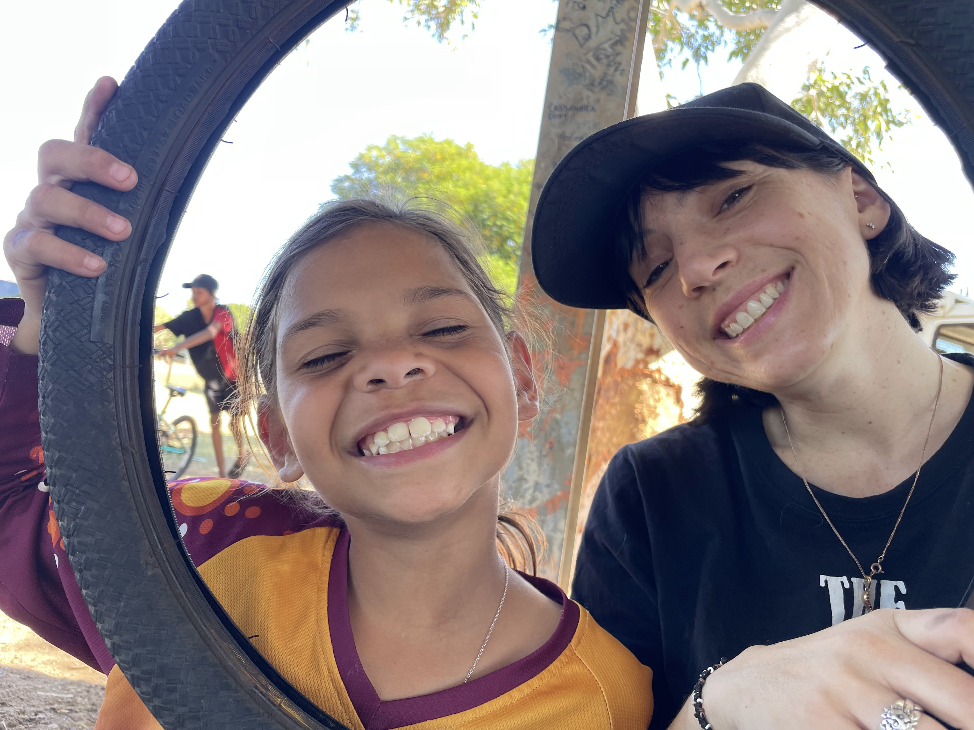 Girl and woman smiling through bike wheel